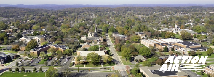 Aerial view of a suburban neighborhood with tree-lined streets, homes, and buildings in a small town.