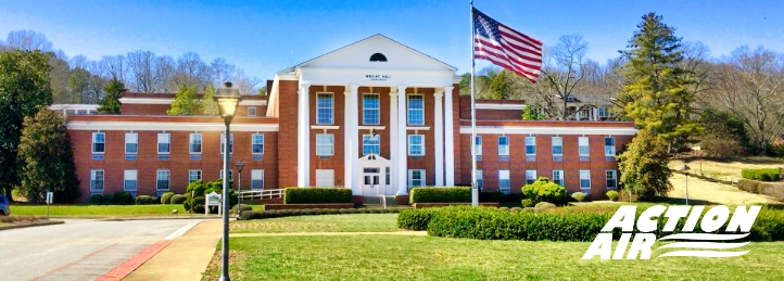 Front view of a brick school building with white columns and an American flag on the lawn.