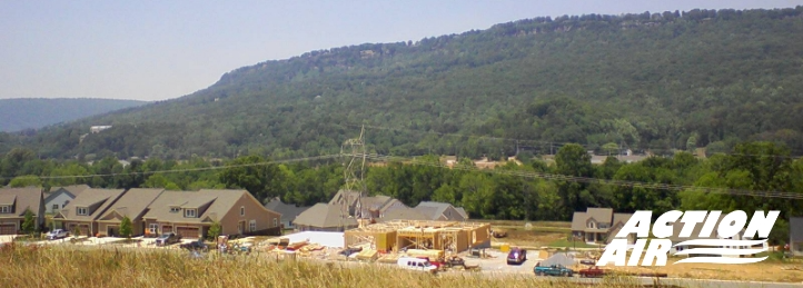 Residential construction site with new homes being built in a valley surrounded by green hills.